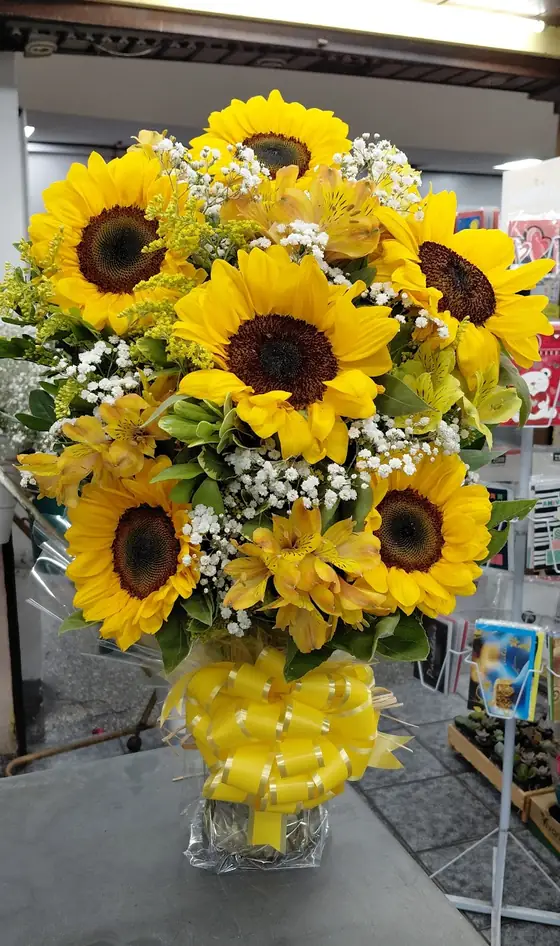Arranjo de girassóis num vaso de vidro com laço amarelo, no balcão da loja